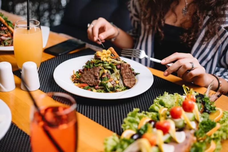 Mulher faz refeição com carne e salada em restaurante.