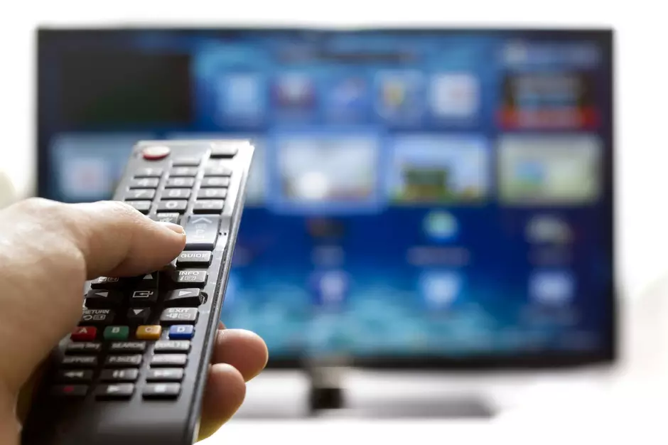 Pessoa utiliza controle remoto diante de uma Smart TV; recurso permite configurar atalhos para aplicativos e outras funções.