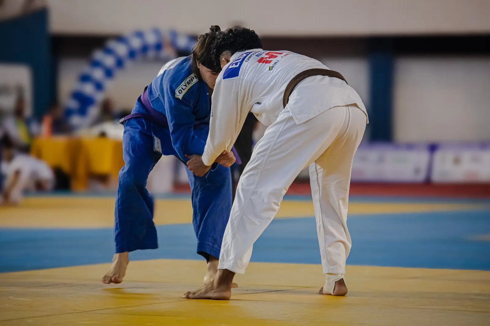 : Dois atletas praticam judô durante uma luta sobre o tatame.