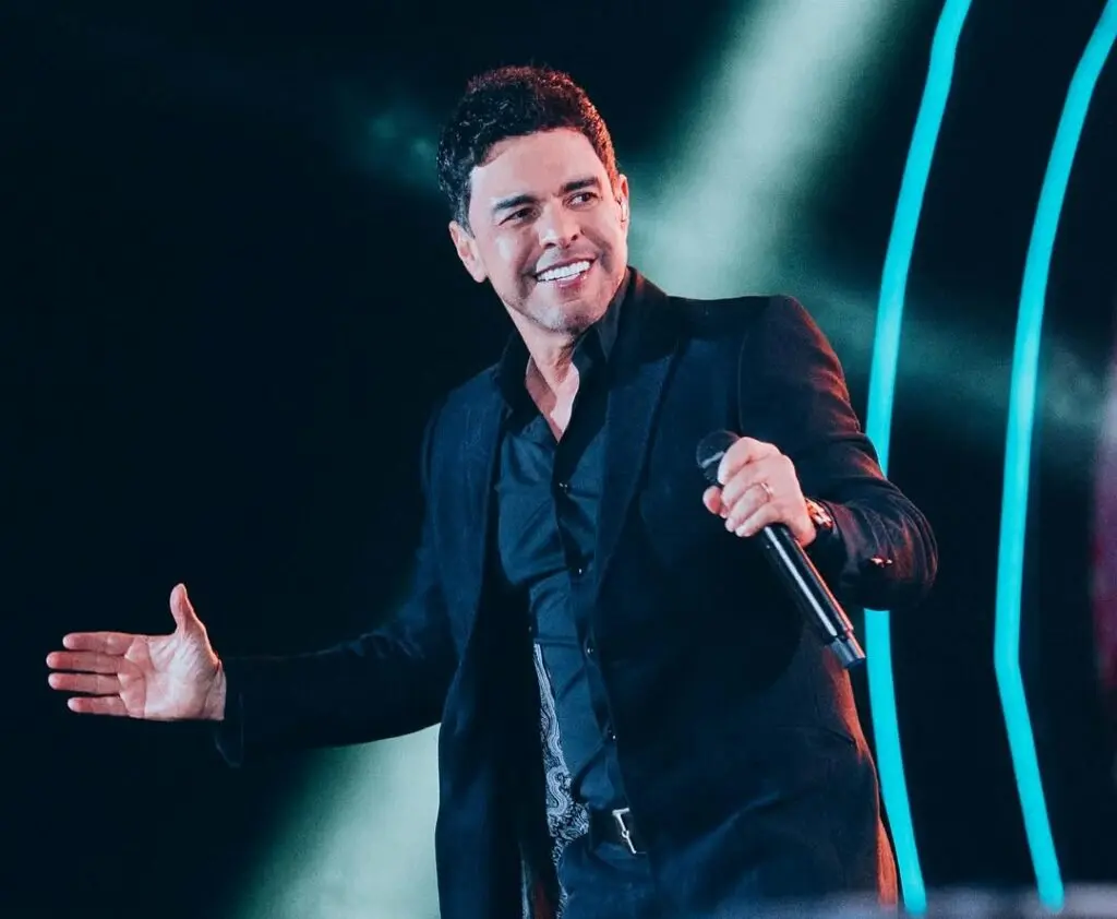 Cantor sertanejo se apresenta no palco, sorrindo e segurando um microfone.