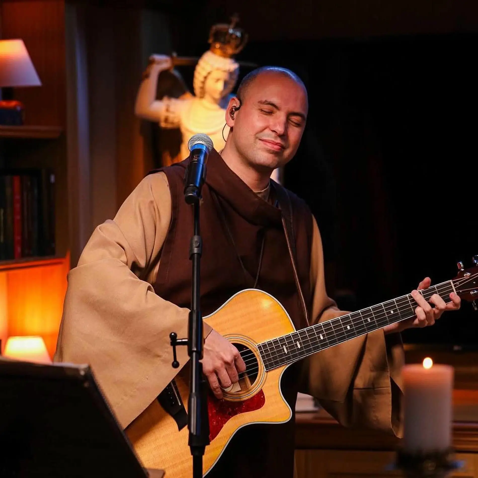 Religioso toca violão durante apresentação musical em ambiente de oração.