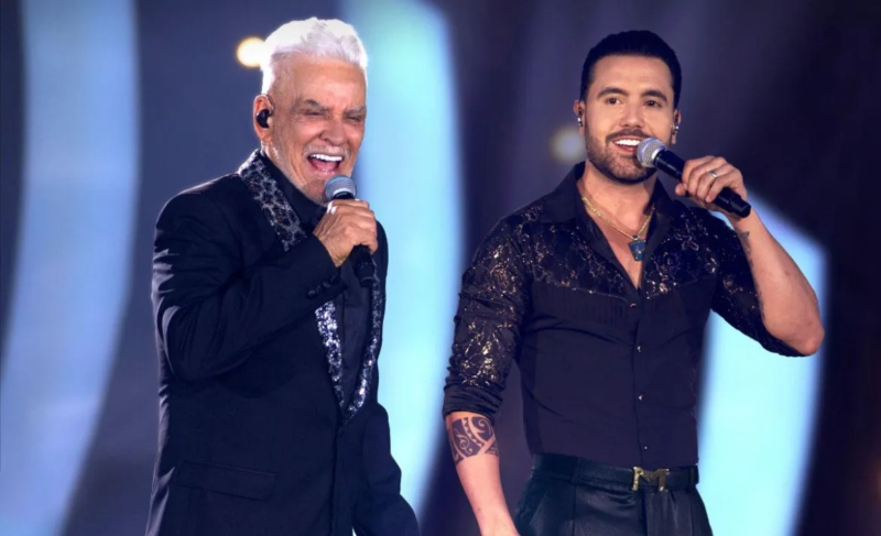 Dois cantores sertanejos se apresentam juntos no palco, segurando microfones durante um show.