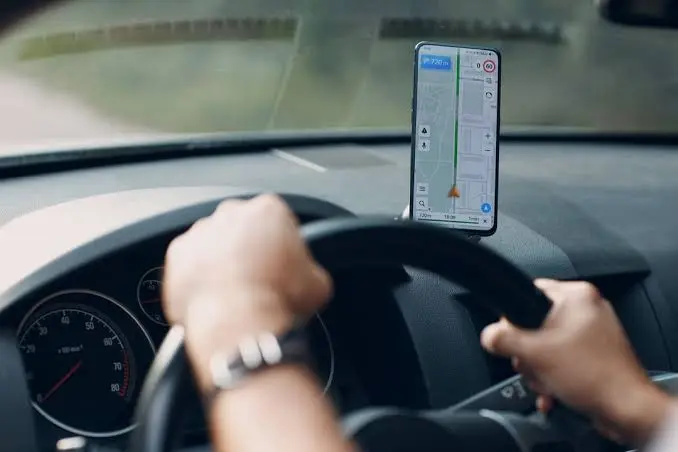 Motorista de aplicativo dirige veículo com celular exibindo aplicativo de navegação.