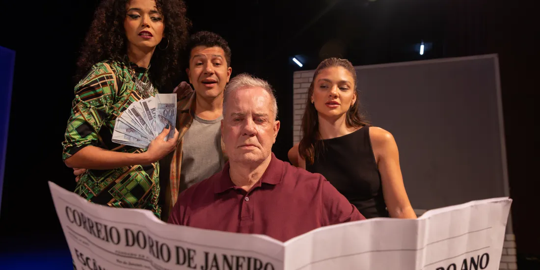 Cena da peça “Baixa Sociedade” mostra quatro atores no palco, com dinheiro e jornal em destaque.