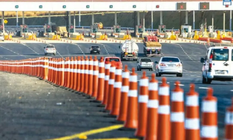 Praça de pedágio em rodovia com veículos passando pelas cabines de cobrança.