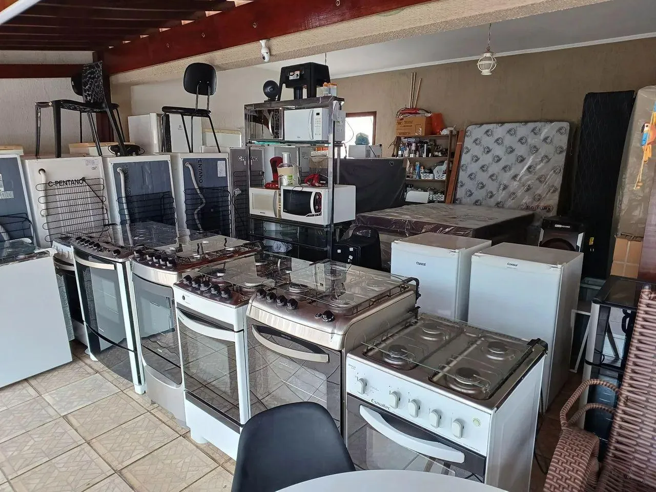 Fogões, geladeiras, micro-ondas, colchões e cadeiras reunidos em um espaço coberto.