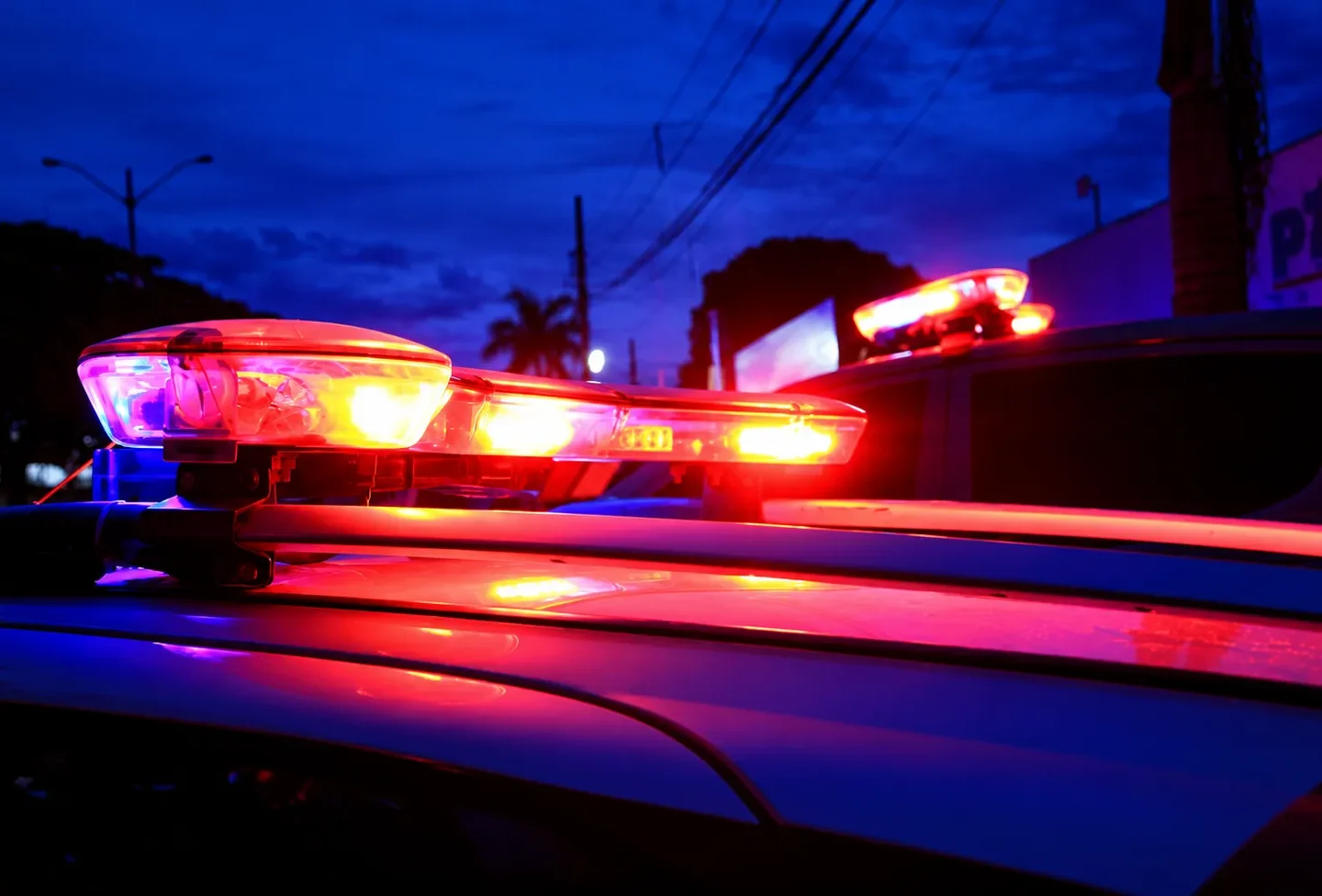 Luzes de emergência vermelhas e azuis acesas sobre viaturas policiais ao anoitecer.