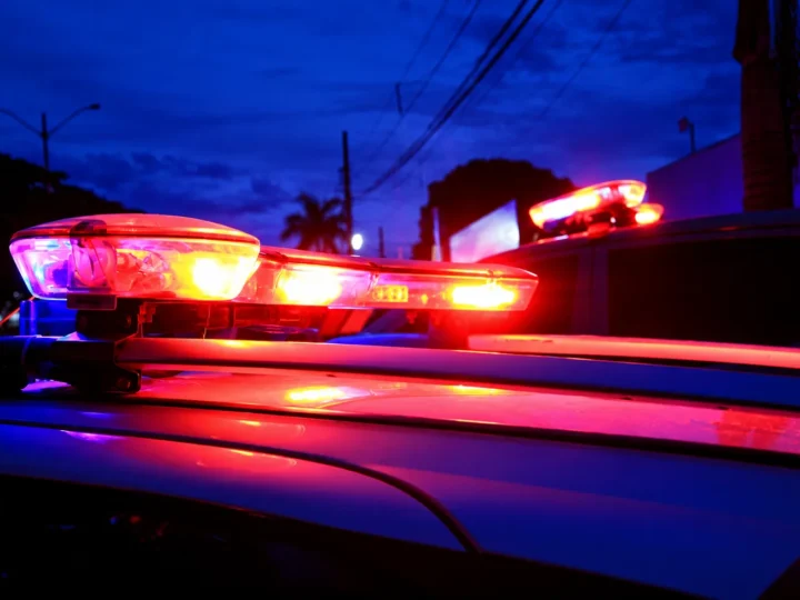 Luzes de emergência vermelhas e azuis acesas sobre viaturas policiais ao anoitecer.