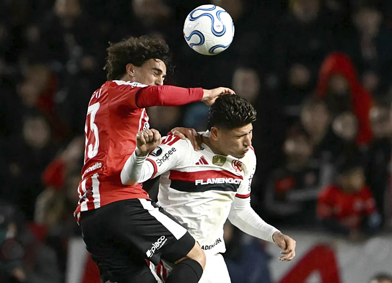 : Jogadores de Flamengo e Estudiantes disputam uma bola pelo alto durante uma partida.