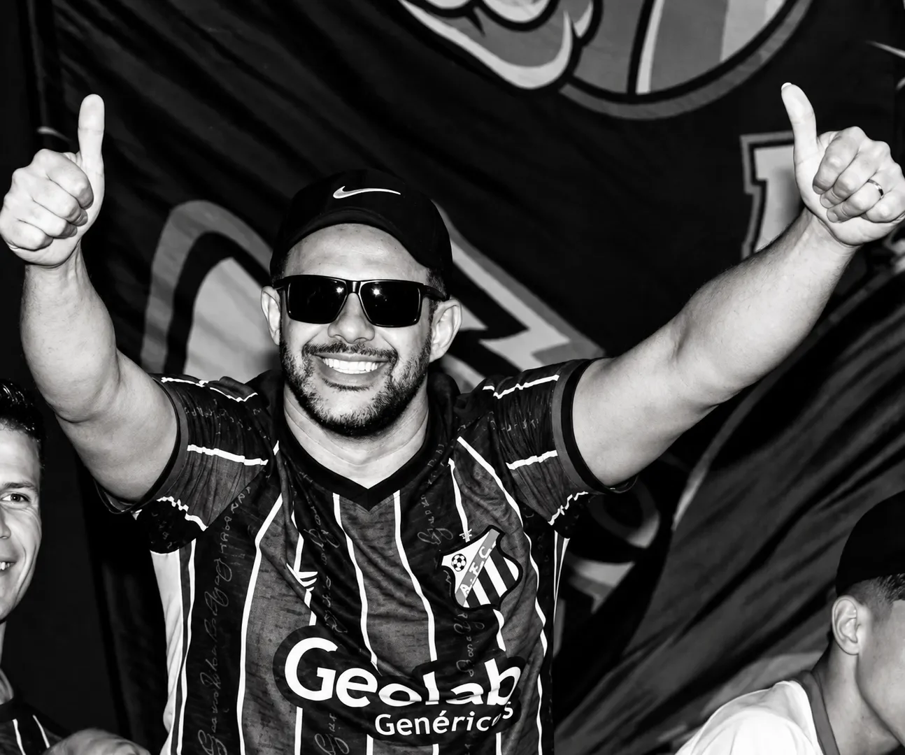 Rodrigo Costa Teixeira sorri com os braços levantados e os polegares para cima, usando boné, óculos escuros e camisa do Anápolis Futebol Clube.