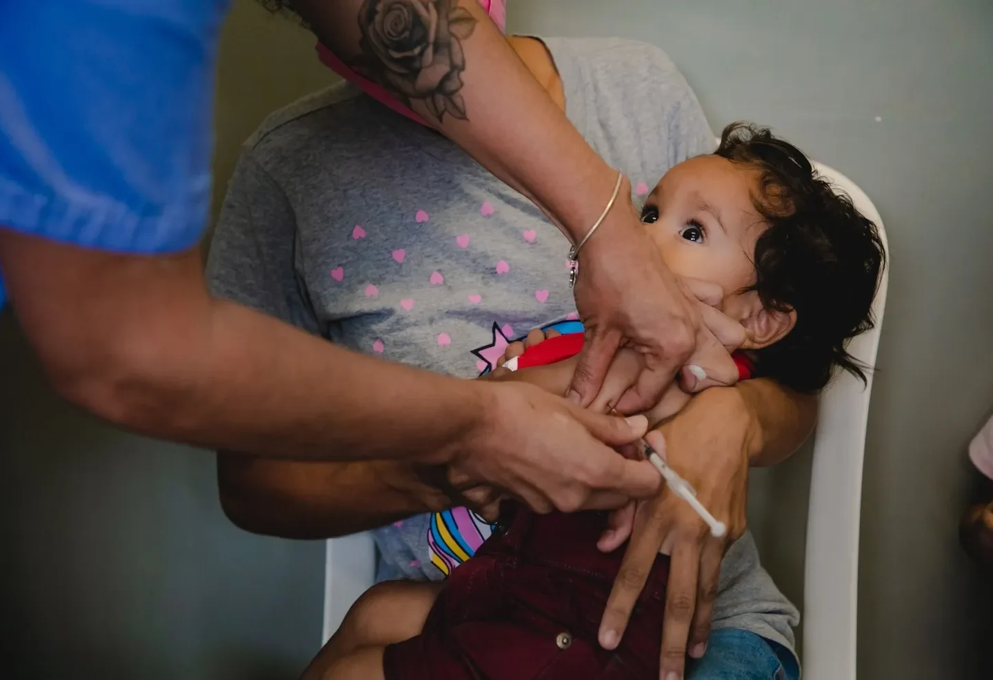 Profissional de saúde aplica uma vacina no braço de uma criança no colo de uma mulher