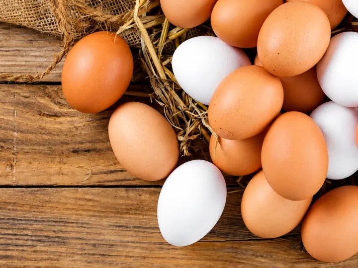 Ovos brancos e marrons sobre palha e uma superfície de madeira.