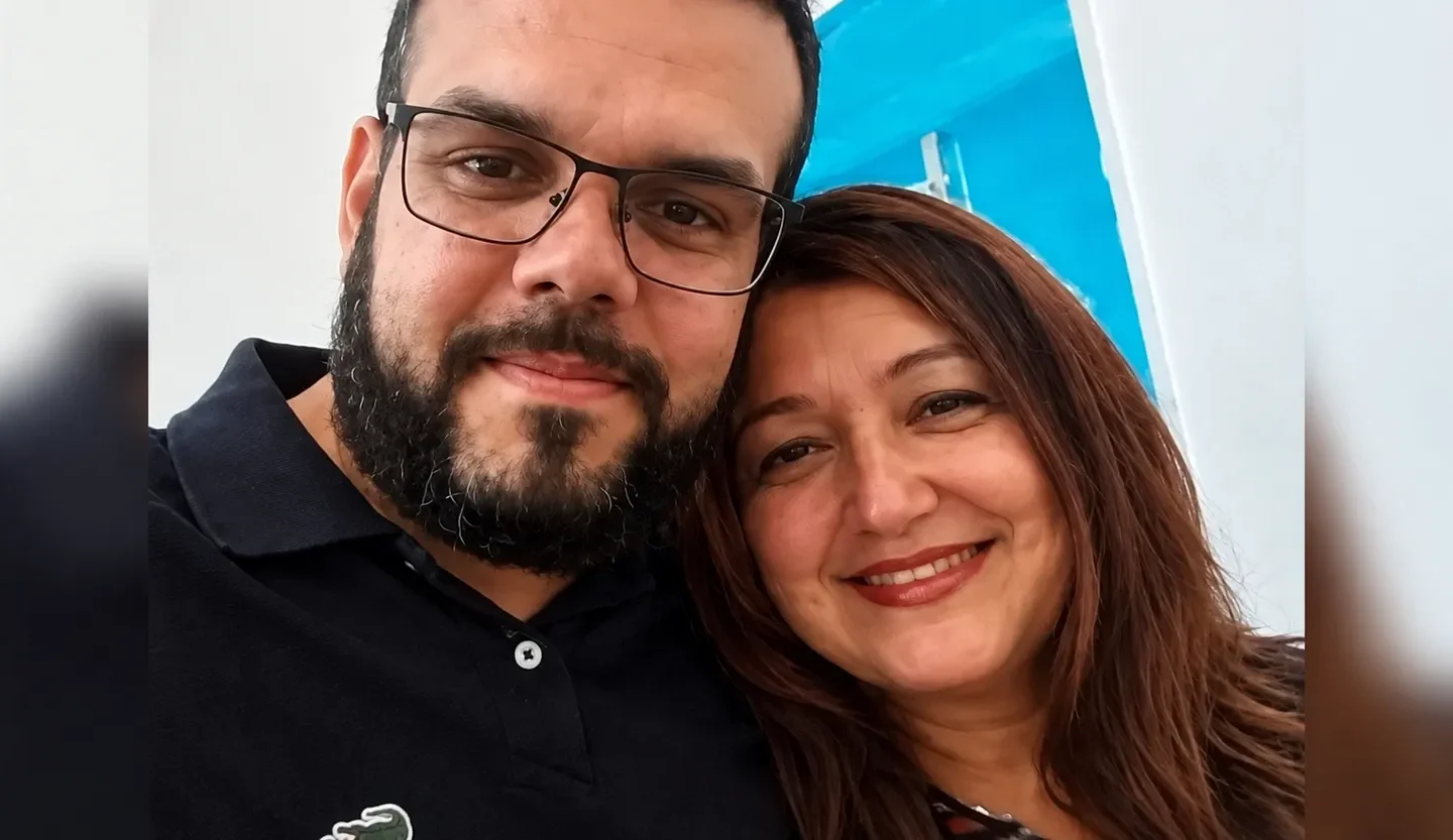 Homem de óculos e camisa preta ao lado de uma mulher de cabelos castanhos, ambos sorrindo para uma selfie