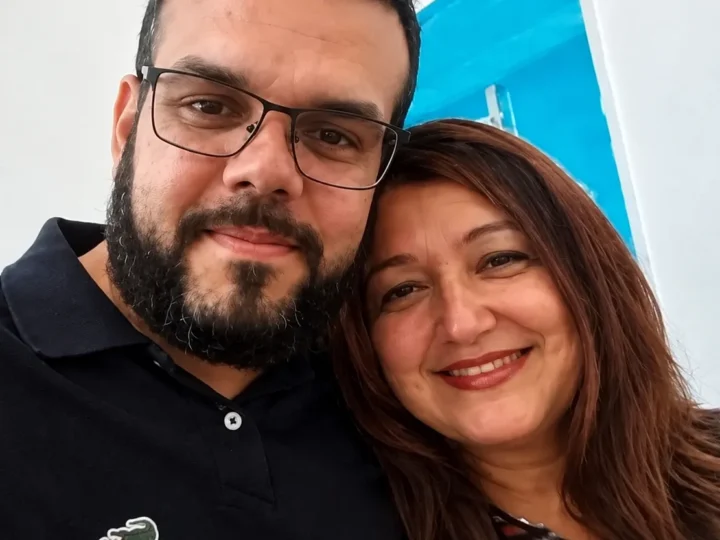 Homem de óculos e camisa preta ao lado de uma mulher de cabelos castanhos, ambos sorrindo para uma selfie