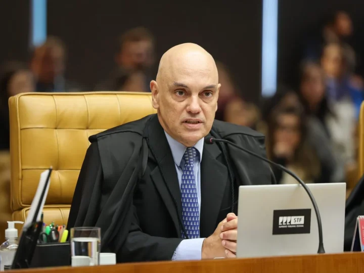 Alexandre de Moraes sentado no plenário do STF, diante de um microfone e de um notebook.