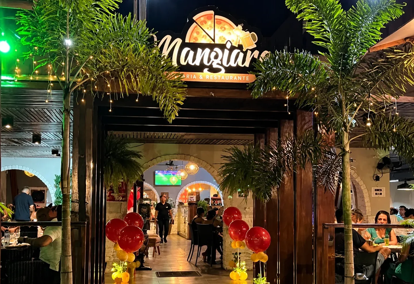 Fachada iluminada da Mangiare Pizzaria & Restaurante, em João Pessoa, com clientes nas mesas.