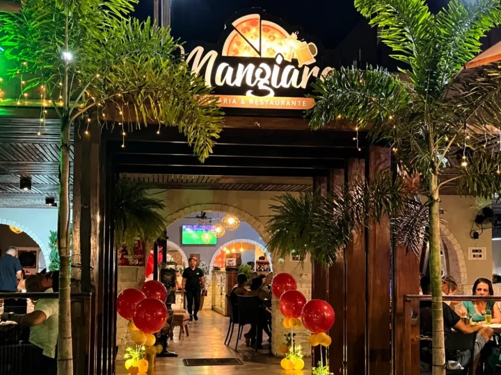 Fachada iluminada da Mangiare Pizzaria & Restaurante, em João Pessoa, com clientes nas mesas.