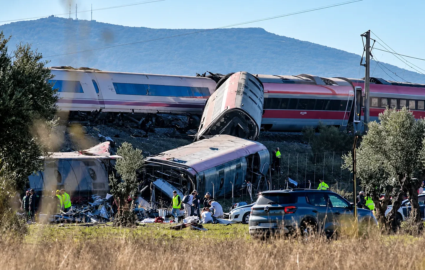 Vagões de trem descarrilados e danificados, com equipes de resgate e veículos de emergência ao redor
