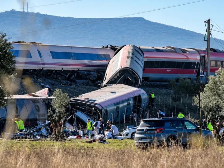 Vagões de trem descarrilados e danificados, com equipes de resgate e veículos de emergência ao redor
