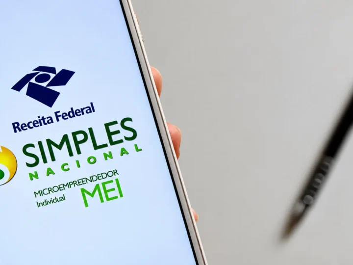 Celular exibe os logotipos da Receita Federal, do Simples Nacional e do MEI, com uma caneta desfocada ao fundo.