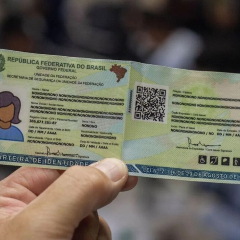 Mão segura modelo ilustrativo da Carteira de Identidade Nacional, com QR Code e dados fictícios.Mão segura modelo ilustrativo da Carteira de Identidade Nacional, com QR Code e dados fictícios.