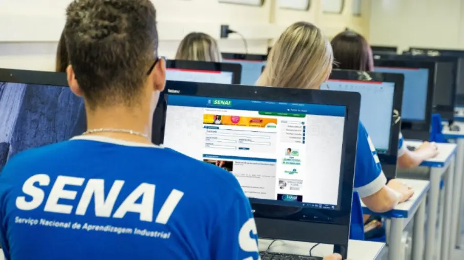 Alunos com camisetas do Senai utilizam computadores em uma sala de informática.