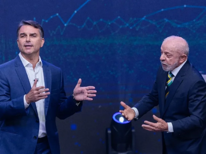 Flávio Bolsonaro, à esquerda, e Lula, à direita, gesticulam durante debate em cenário azul