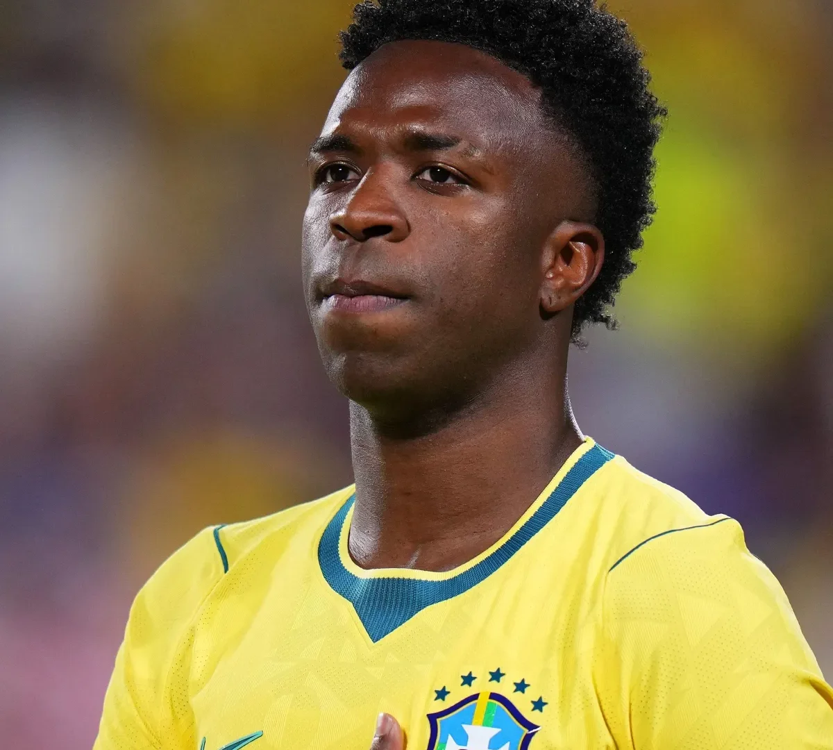 Vini Jr. com a camisa amarela da seleção brasileira e a mão sobre o peito