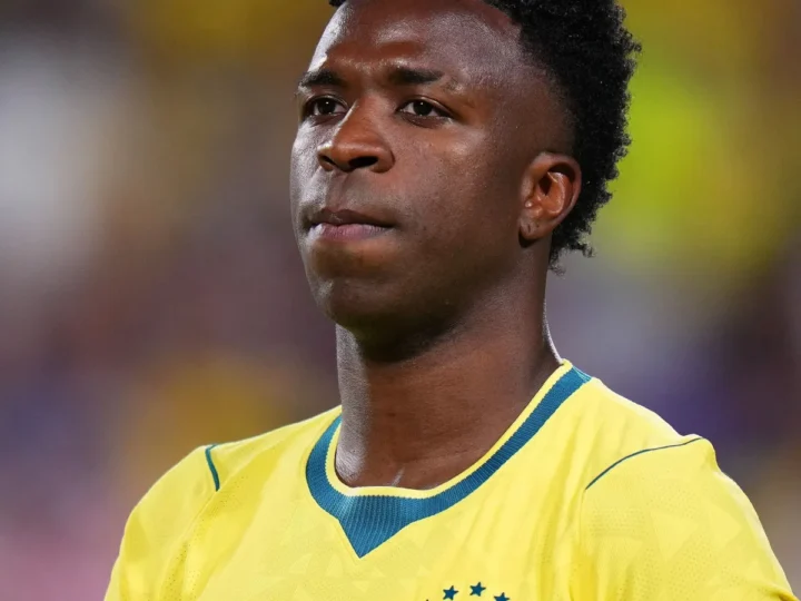 Vini Jr. com a camisa amarela da seleção brasileira e a mão sobre o peito